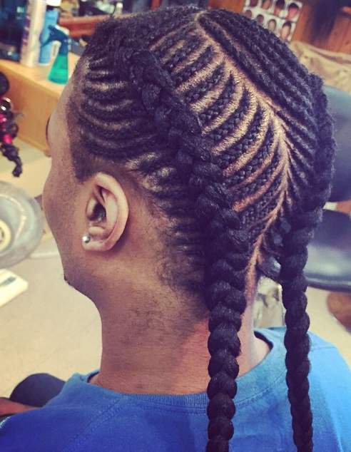 A picture of a black guy with a long cornrows hairstyle braided through his kinky curly hair at a barbershop