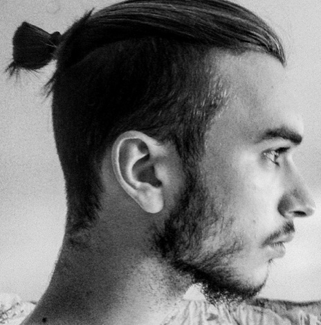 A black and white photograph of a young man with a hip topknot undercut hairstyle