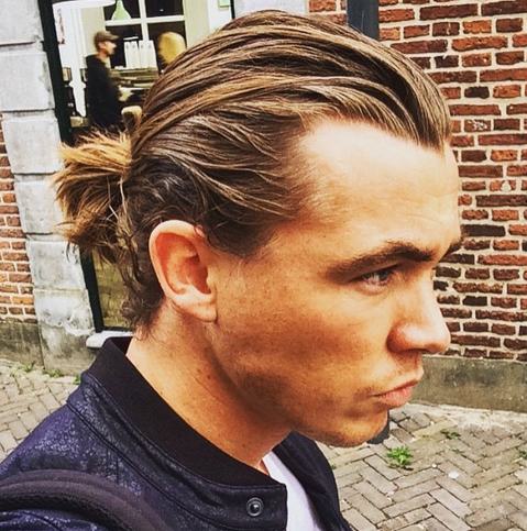 A photo of a handsome blond male with long hair and a low manbun hairstyle