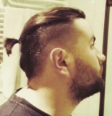A photo of a middle-aged guy with a Samurai hairstyle with a taper haircut and stubble