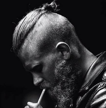 A photograph of a sexy hipster male model with a topknot undercut hairstyle and a thick beard smoking tobacco