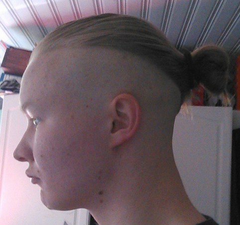A picture of a young kid with a man bun undercut shaved on the sides and back of his blond long hair