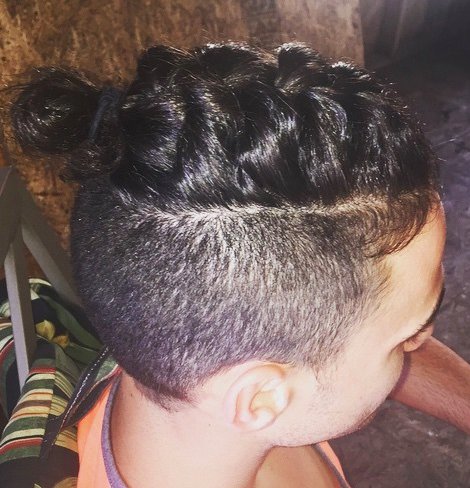 A photograph of a young curly boy with a topknot undercut hairstyle and a braided bun