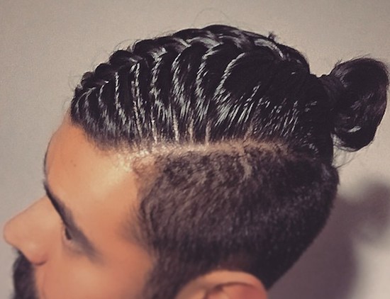 A picture of a black male with a man bun undercut hairstyle that has been braided with a slicked pomade for a high-shine texture
