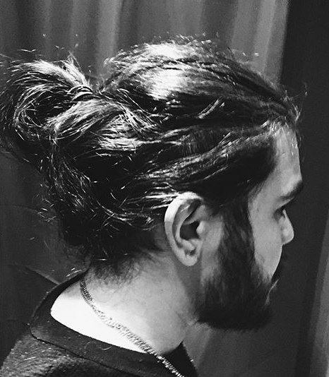 A black-and-white photograph of an Indian male with hipster beard and a loose man bun hairstyle that protects him from traction alopecia and a receding hairline
