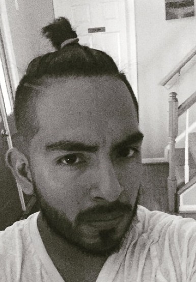 A photo of a hipster with his top knot hairstyle placed on the center of his head as he gets ready to buzz an undercut for the hair on the sides and back