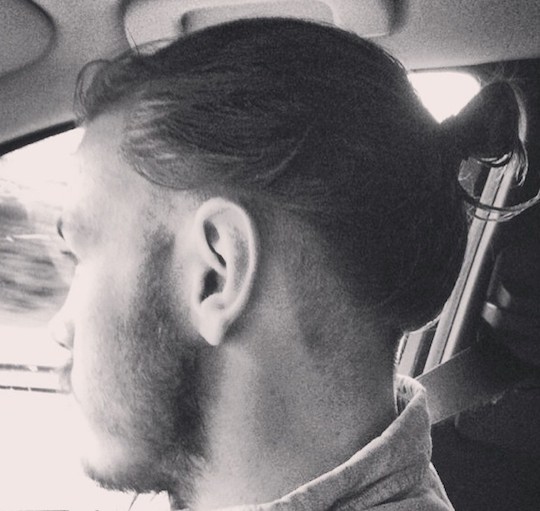 A photograph of a German male with a man bun undercut hairstyle placed low on the sides and back of his head