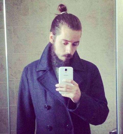 A photograph of a long hair male with a full manbun hairstyle posing in front of the mirror