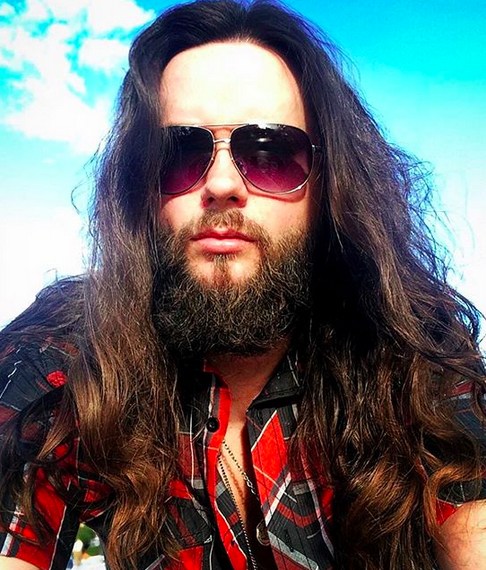A photo of a male hipster wearing sunglasses with a bushy full beard and very long wavy hair in a messy hairstyle