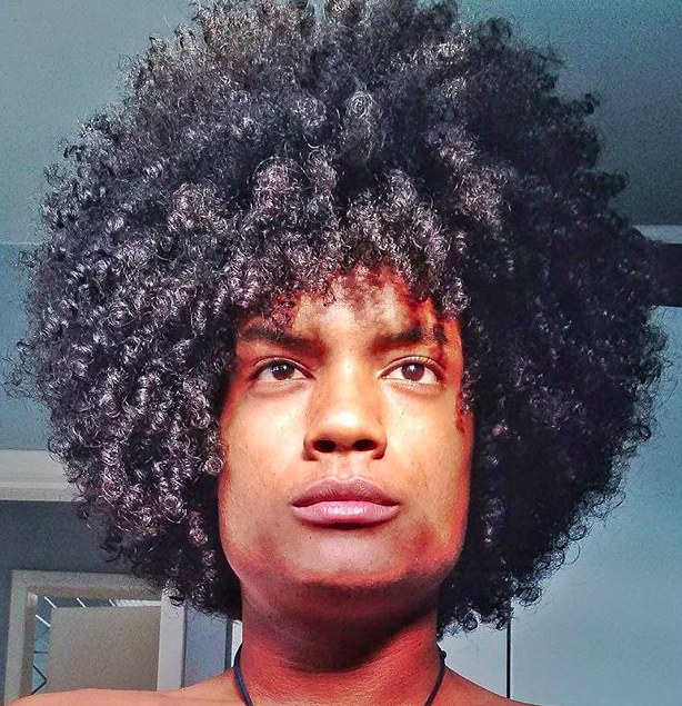 A photograph of a black guy with a beautiful afro hairstyle achieved by using a conditioner and a hair pick for his kinky curls