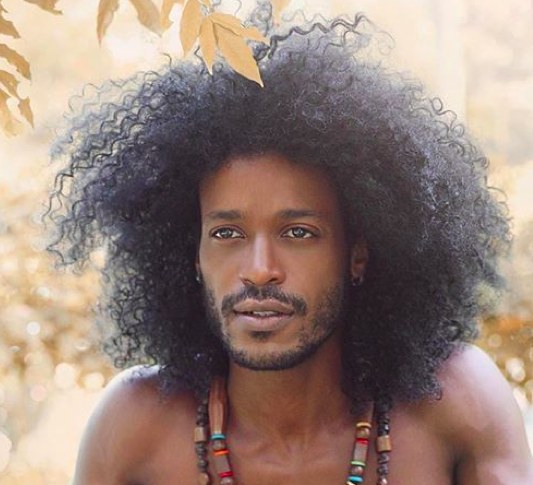 A photograph of a black male with his long curly hair in a huge afro hairstyle