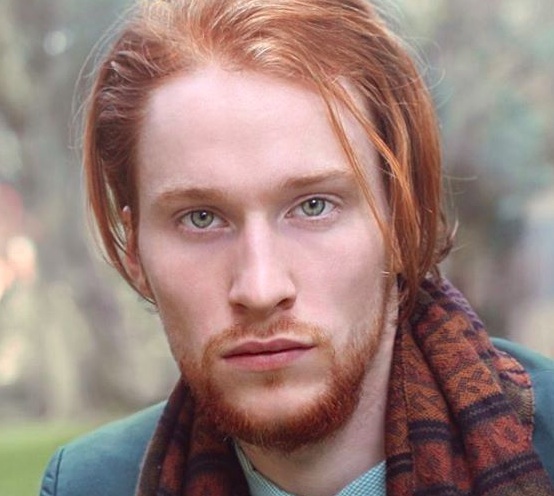 A photograph of a redhead male model with a slicked back hairstyle achieved by using a water based pomade for a cool wet-hair look