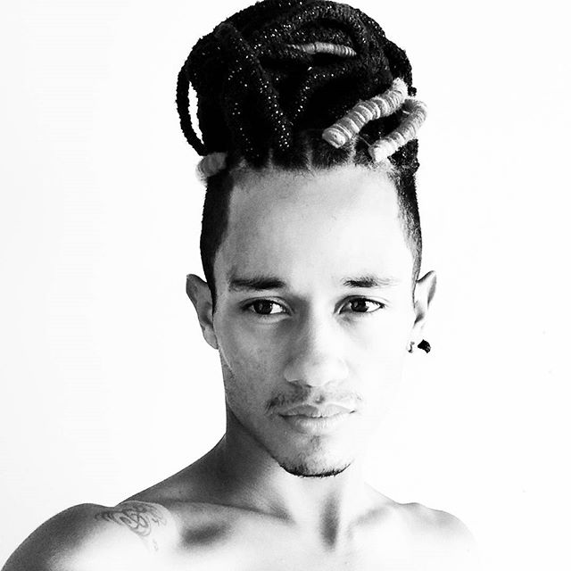 A photograph of a black guy with his cool long curly hair styled as dreadlocks with a fade haircut