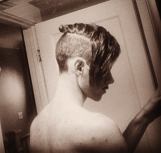 A picture of a young man with his long blonde hair styled into a top knot undercut hairstyle