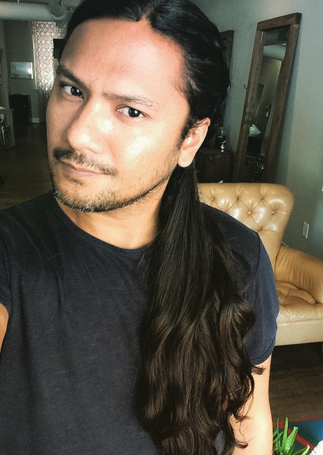 A photograph of a Filipino male with long curly hair that has been tied into a ponytail hairstyle