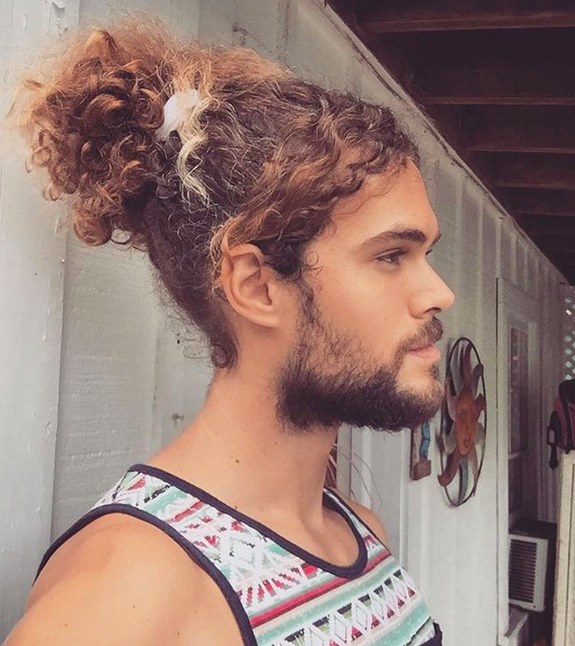 A photograph of a curly male hipster sporting a full beard style and a manbun hairstyle for his epic long mane