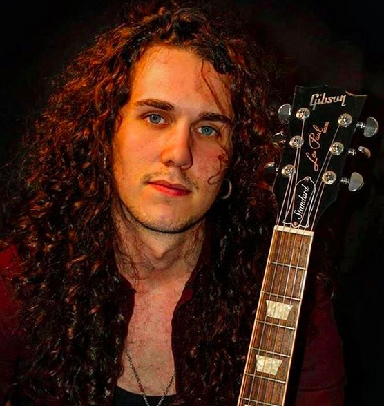 A photograph of a heavy-metal male vocalist with long curly hair styled down with hair mousse and hairstyling spray