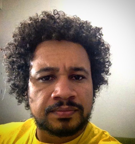 A photograph showing a bearded black male growing his afro curls during the awkward stage of hair growth that affects all men with curly hair