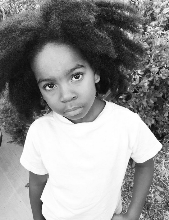A black-and-white picture of an African American boy with his long kinky hair combed as a curly middle-parted hairstyle