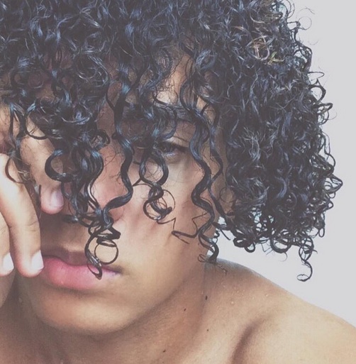 A picture of a mulatto male with wet long curly hair that has been styled as bangs