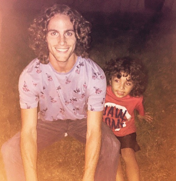A picture of a father with his son playing in the park as they both sport cool middle-parted hairstyles for their long curly hair
