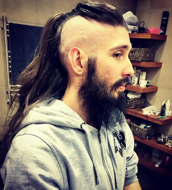 A photograph of a French hipster male with waist-length long hair styled with an undercut haircut that resembles a big Mohawk hairstyle with wavy curls