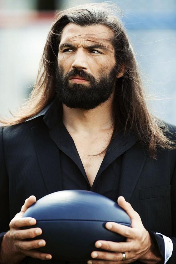 A photograph of a massively-sized bearded male with very long straight hair that has been combed as a side swept hairstyle with a hairstyling cream