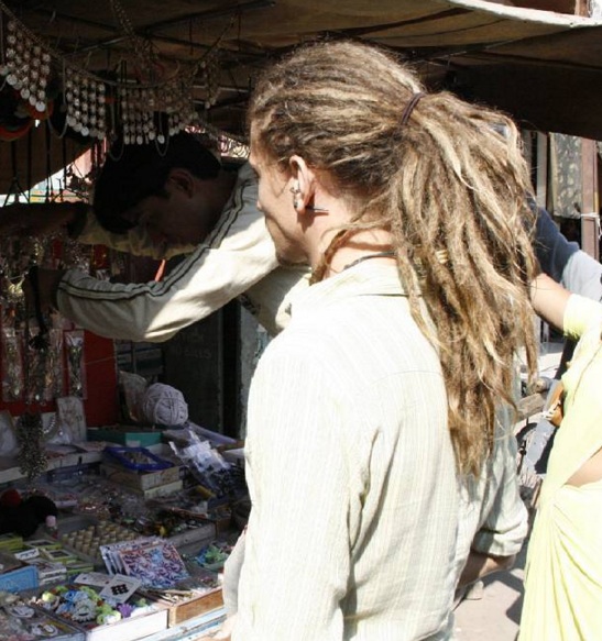 A picture of a Rastafarian white male with super long dreadlocks styled back into a ponytail as he casually walks around Kingston in Jamaica