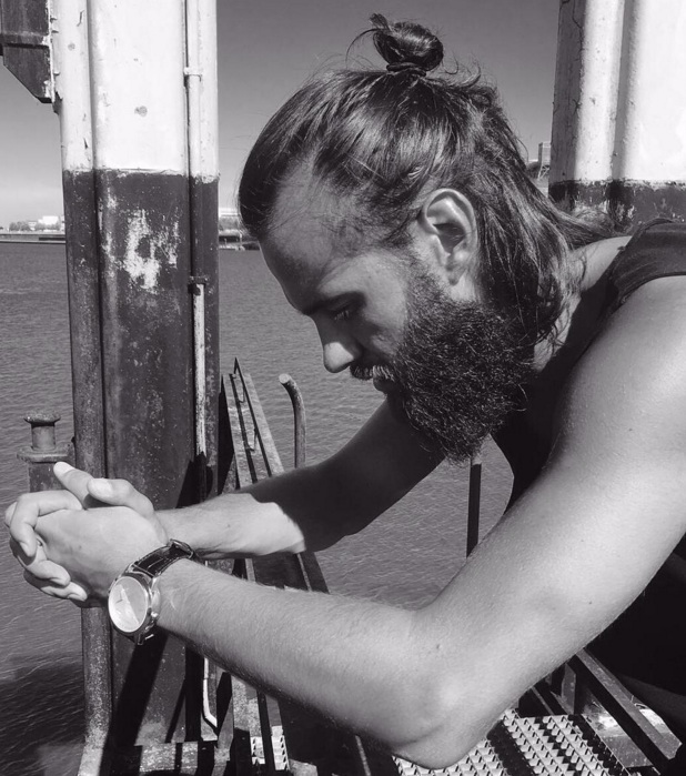 A picture of a bearded hipster with his long hair styled as a manbun hairstyle with a ponybun which leaves the locks in the back of the head dangling over the shoulders