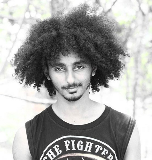 A picture of an Arab-American hipster with long curly hair styled with a shaggy haircut and combined with a beard-stubble style