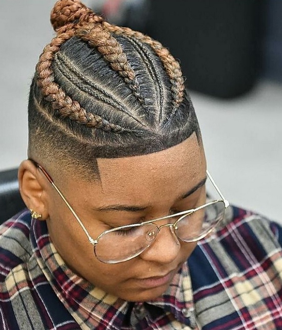 A barbershop photograph of a black male with his long blonde hair braided into a manbraid hairstyle and trimmed with a fade haircut while his hairline has been shaped up