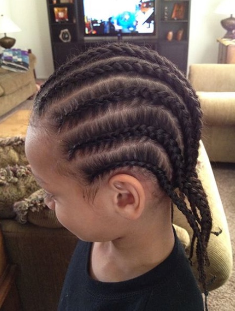 A photograph of a cute mixed-race boy with long hair that has been braided into a cornrows hairstyle and which dangles over his shoulders