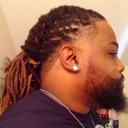 A photograph of an African American male with long hair sported as dreadlocks combined with a temple fade haircut across his hairline