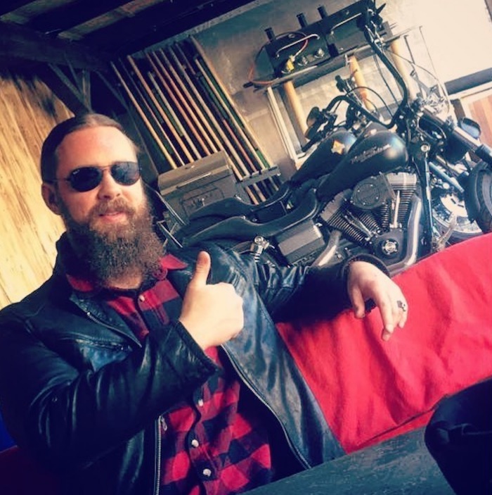A photo of a long hair hipster biker with his Harley Davidson motorcycles