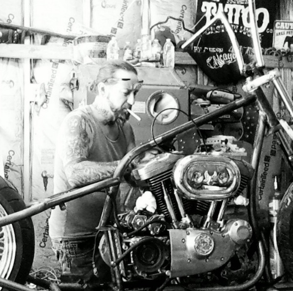 A photo of a long haired manly guy chopping and customizing his Harley Davidson Sportster motorcycle