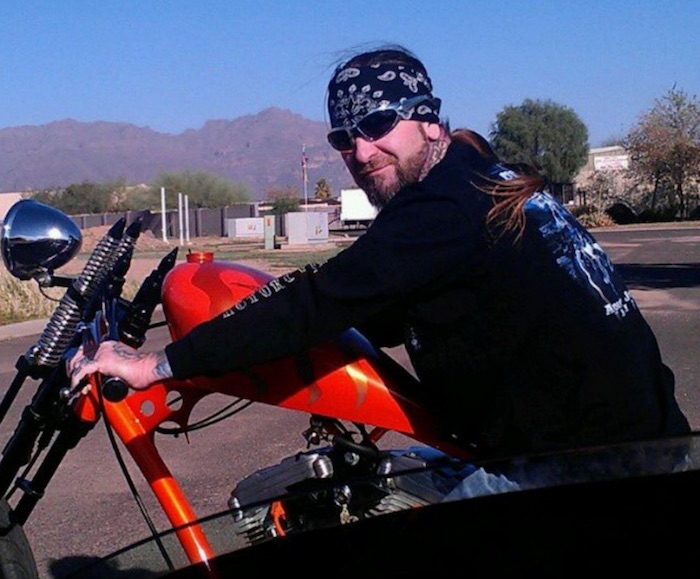 A picture of a Harley Davidson rider with long curly hair pulled back with a bandana and no helmet